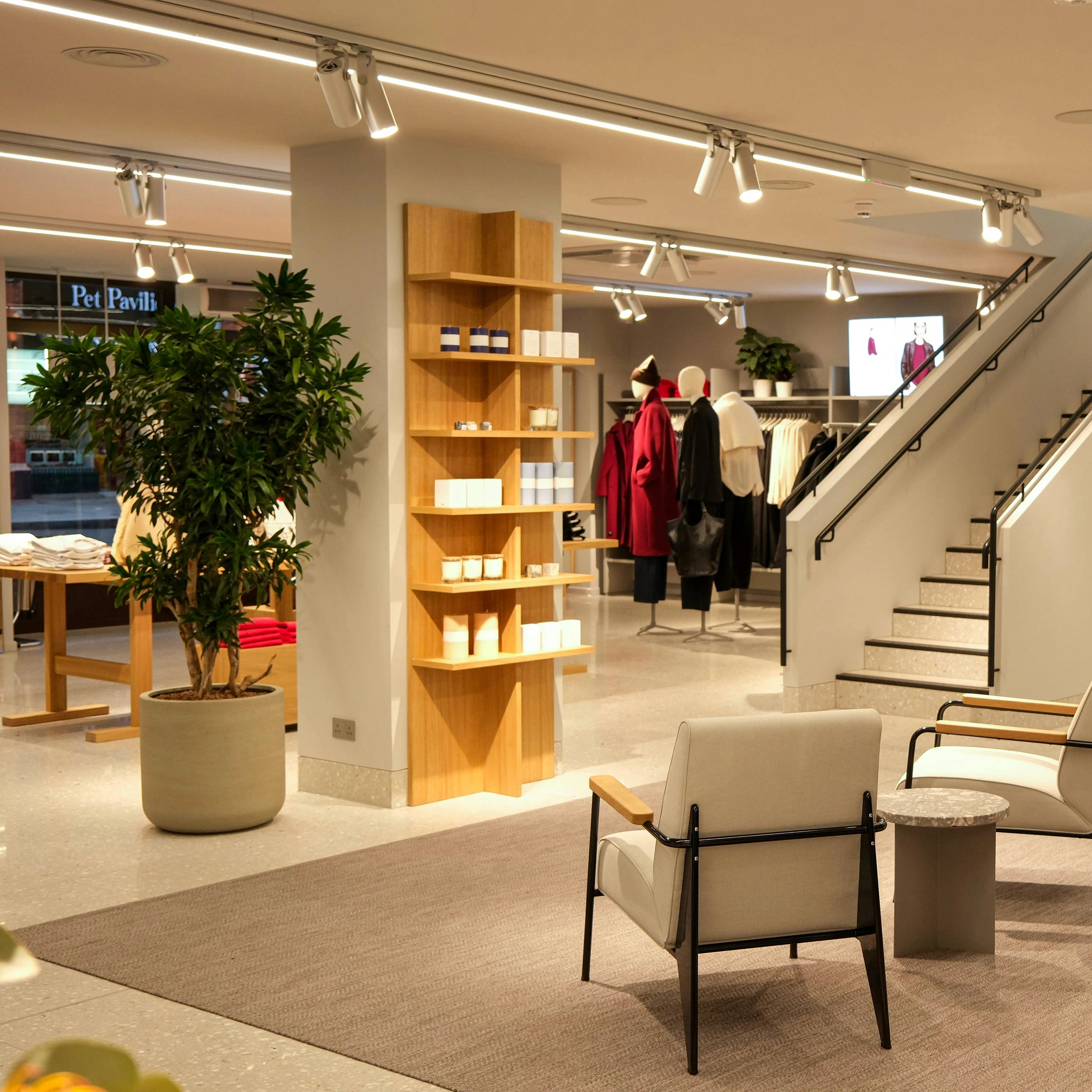 Interior of a modern store with clothing racks, chairs, and a staircase.
