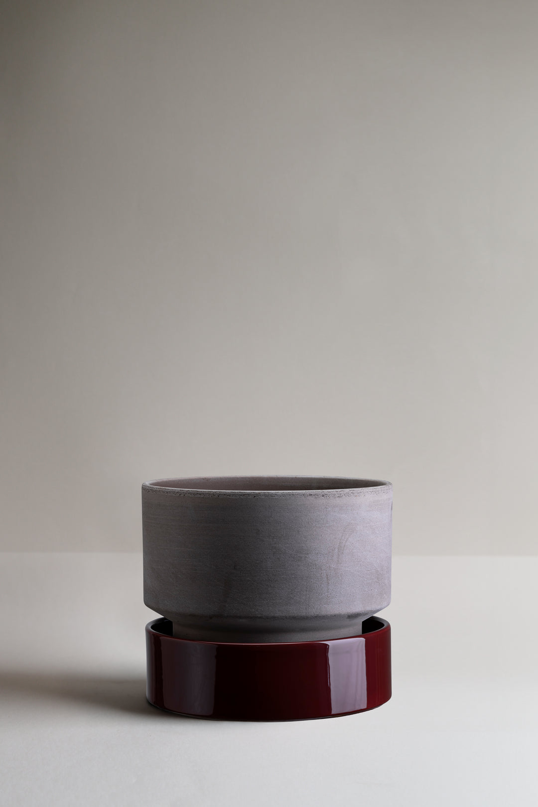 Gray ceramic planter on a dark red stand against a plain background