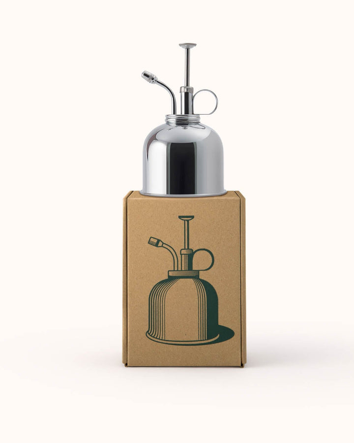 Silver oil dispenser on a cardboard box with a green illustration of an oil dispenser.