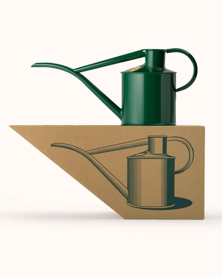 Green watering can on a white background with a cardboard cutout of the same design below.
