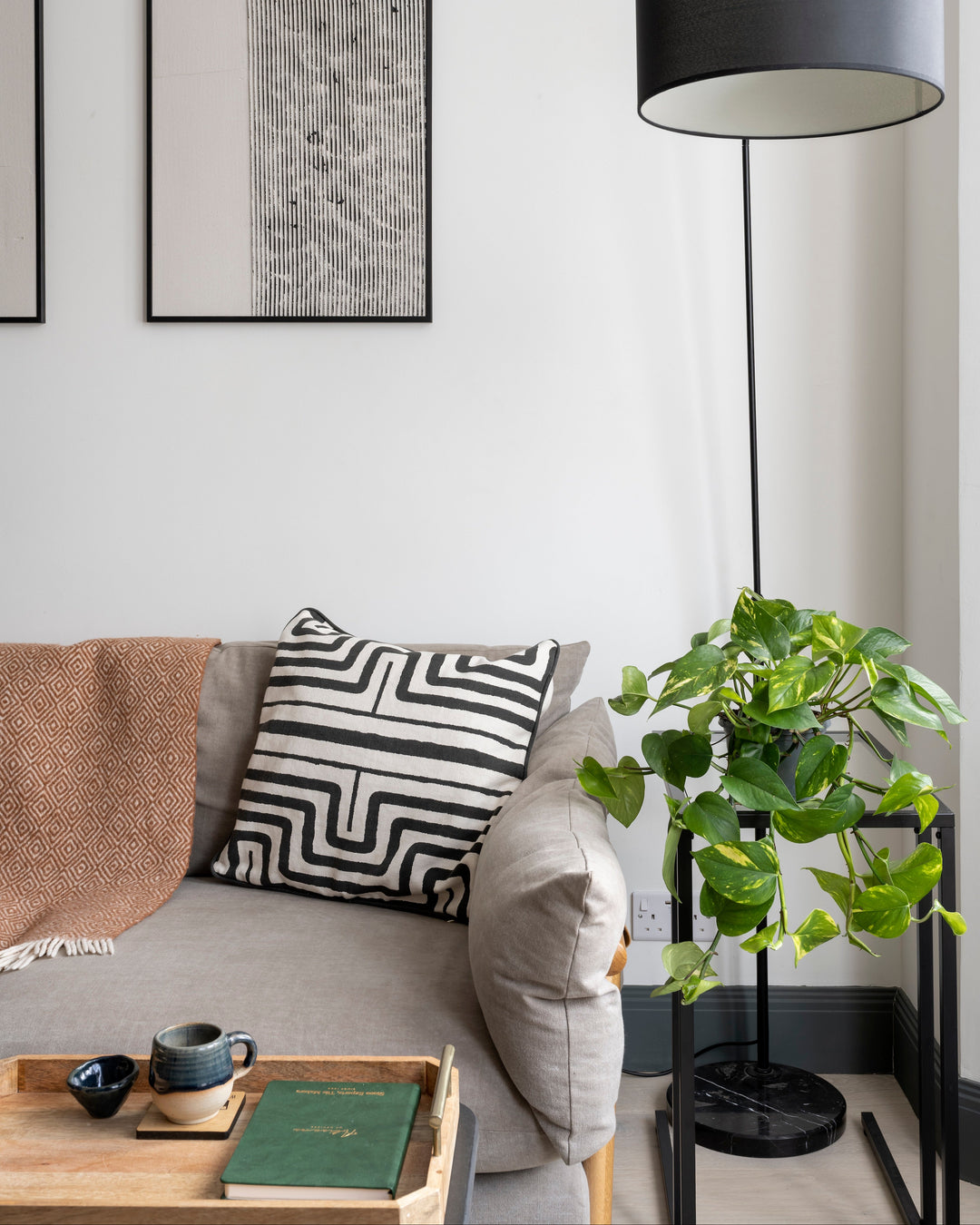 Modern living room with a gray sofa, black floor lamp, and decorative pillows. Devil's ivy by plant drop